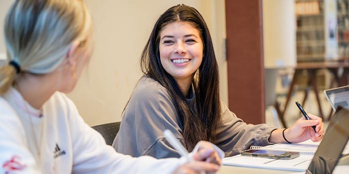 Two students working in library on laptops.