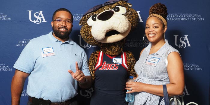 Two people with Ms Pawla smiling in front of USA backdrop.