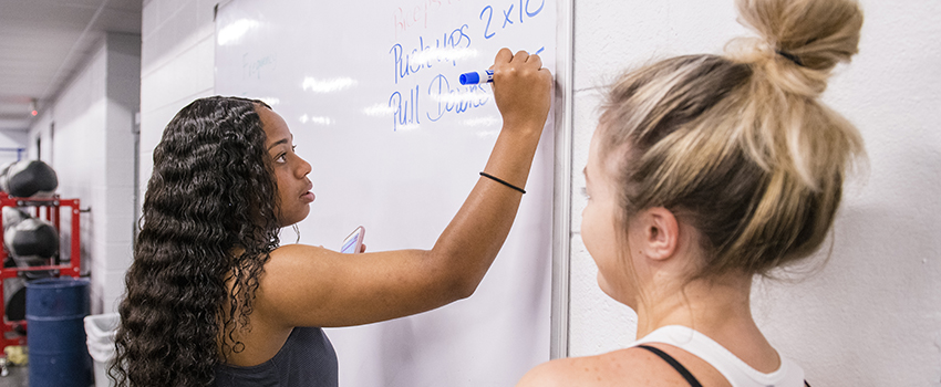 Student writing on board while another student is looking on.