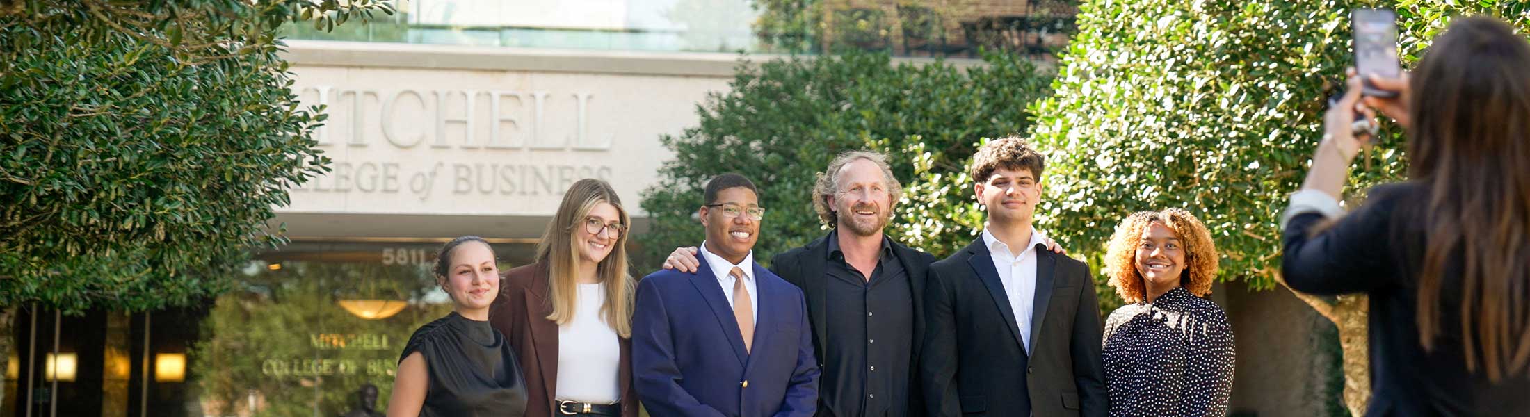 Mitchell Ambassadors in front of MCOB building with someone taking picture.