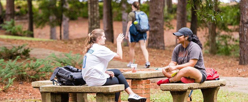 Two South female students sitting outside at tables talking.