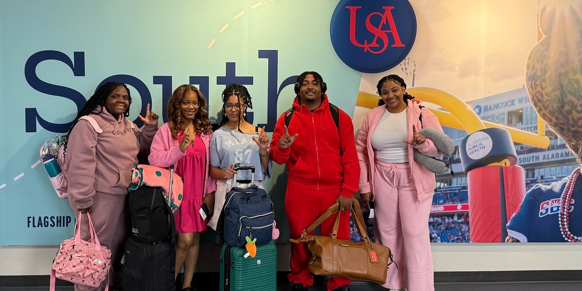 A group of students pose in front of a South Alabama mural at the airport.