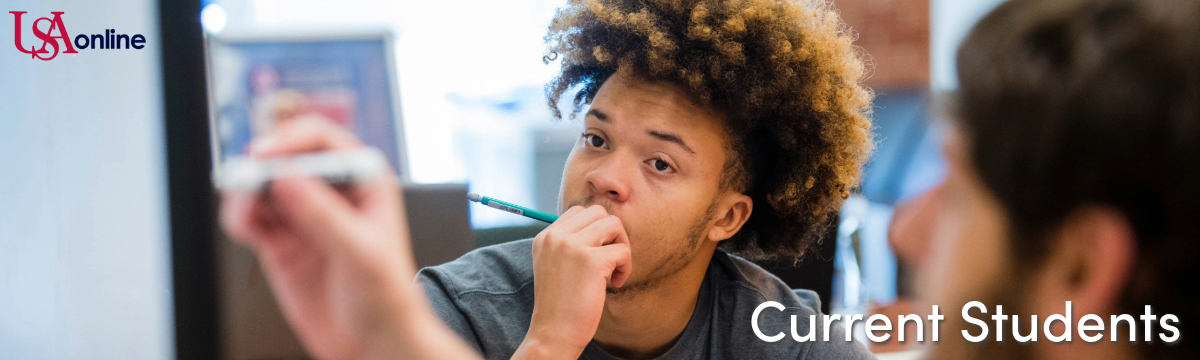 A male student chews on his pencil while watching another male student write on a whiteboard